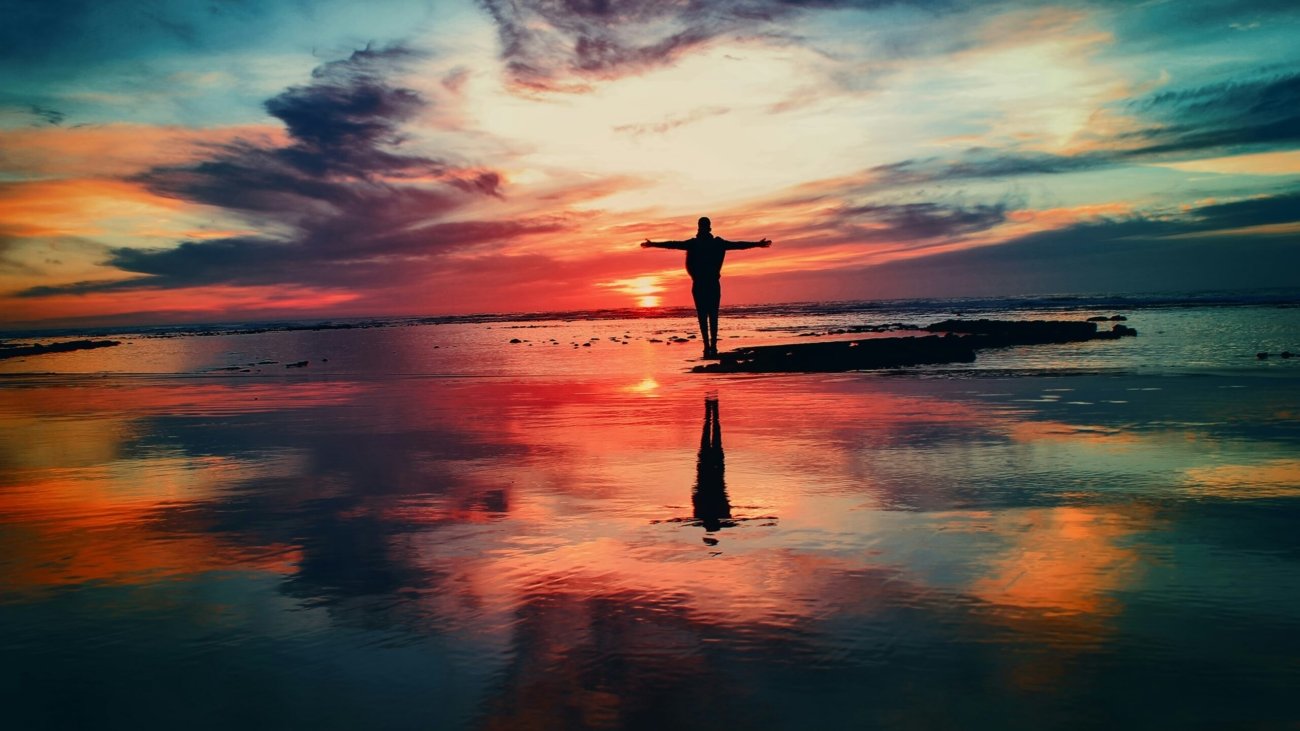 silhouette of person standing on rock surrounded by body of water