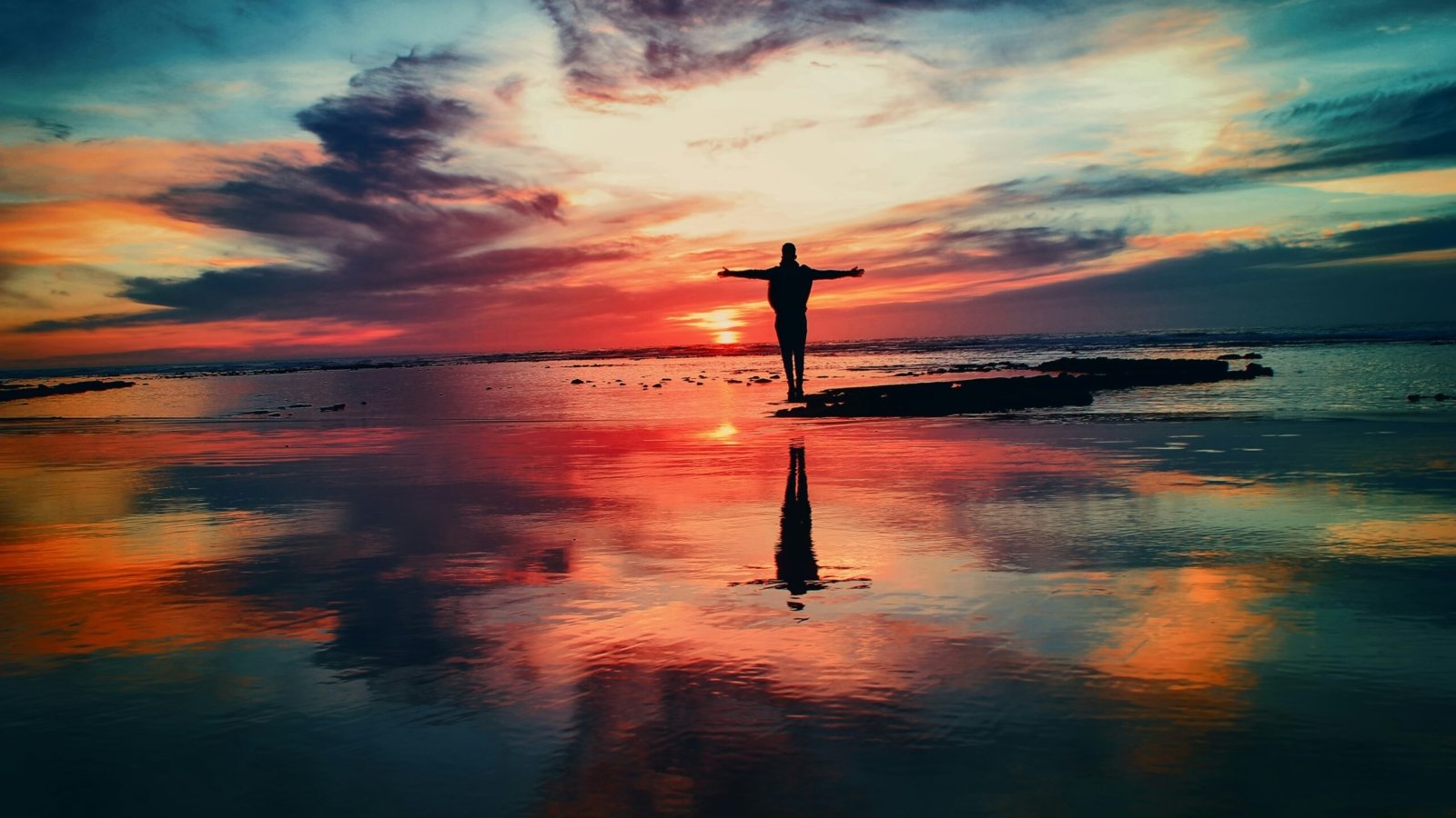 silhouette of person standing on rock surrounded by body of water